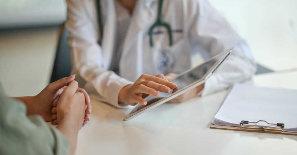 A doctor in a white coat using a digital tablet to show a patient information during a consultation.